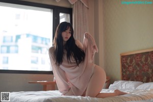 A woman sitting on a bed in a pink sweater.