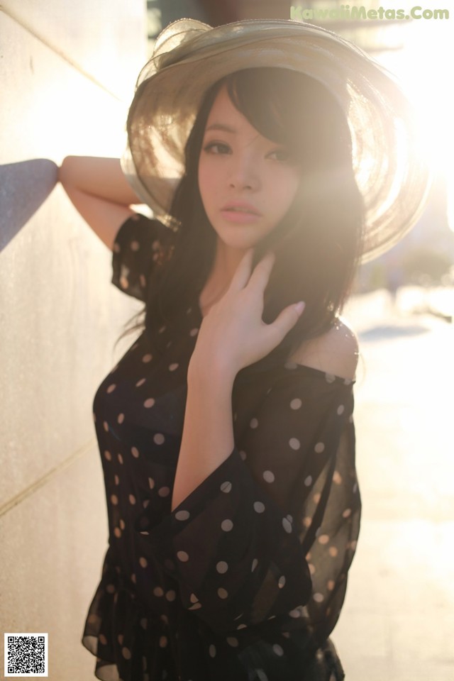 A woman in a black polka dot dress leaning against a wall.