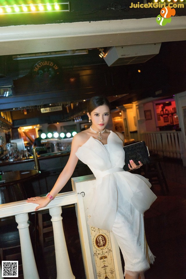 A woman in a white dress standing on a balcony.