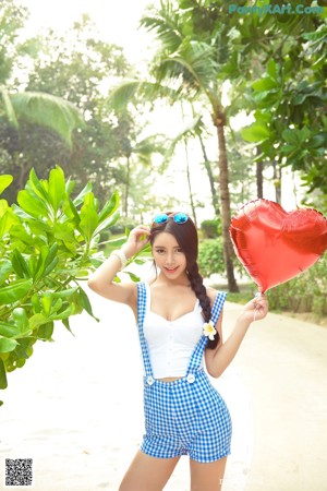 A woman in a blue and white dress holding a red heart shaped balloon.