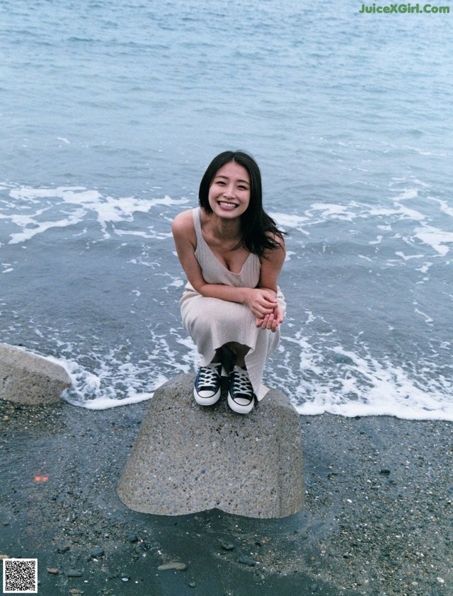 A woman sitting on a rock by the ocean.