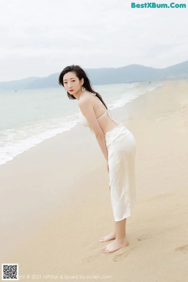 A woman in a white dress standing on a beach.