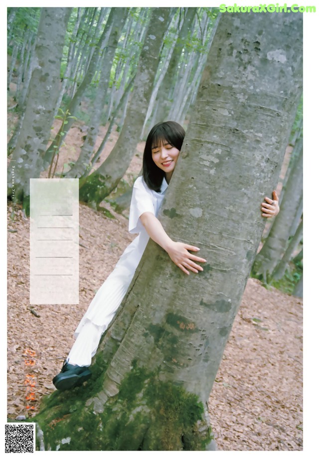 A woman leaning against a tree in a forest.