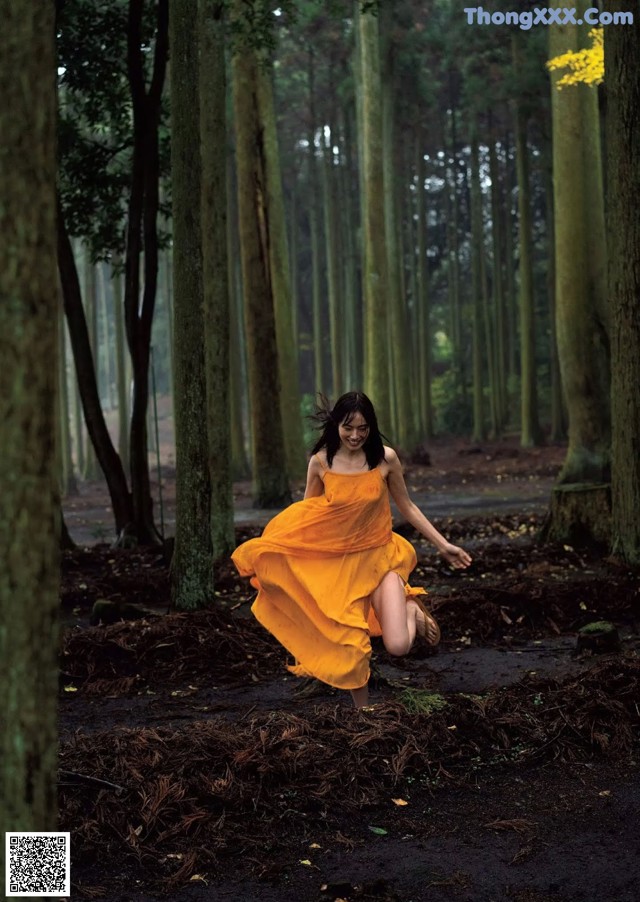 A woman in a yellow dress running through a forest.