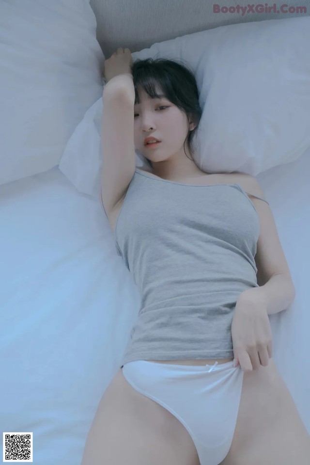 A woman laying on a bed in a gray tank top and white panties.