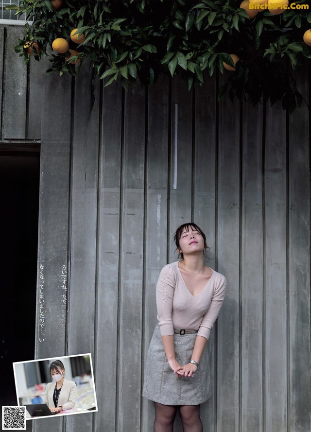 A woman standing in front of a wall with oranges hanging from it.