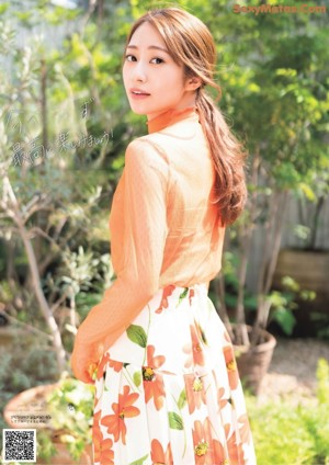 A woman in an orange top and a white skirt posing for a picture.