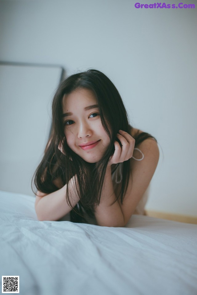 A woman laying on top of a bed with her hand on her chin.