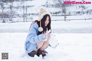 A woman in a blue jacket and white scarf sitting in the snow.