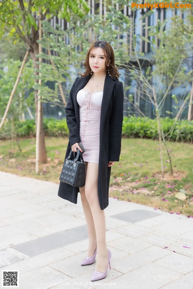 A woman in a pink dress and black coat posing for a picture.