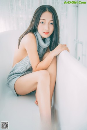 A woman in a gray dress sitting on a white rug.