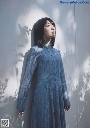 A woman in a blue dress sitting on a window sill.