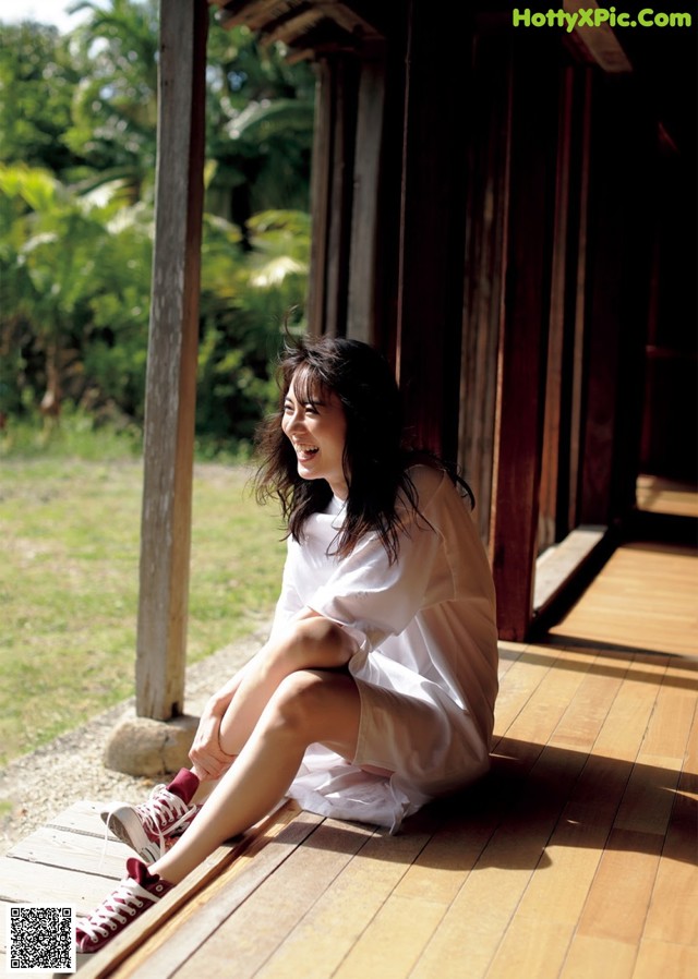 A woman sitting on a wooden porch with her legs crossed.