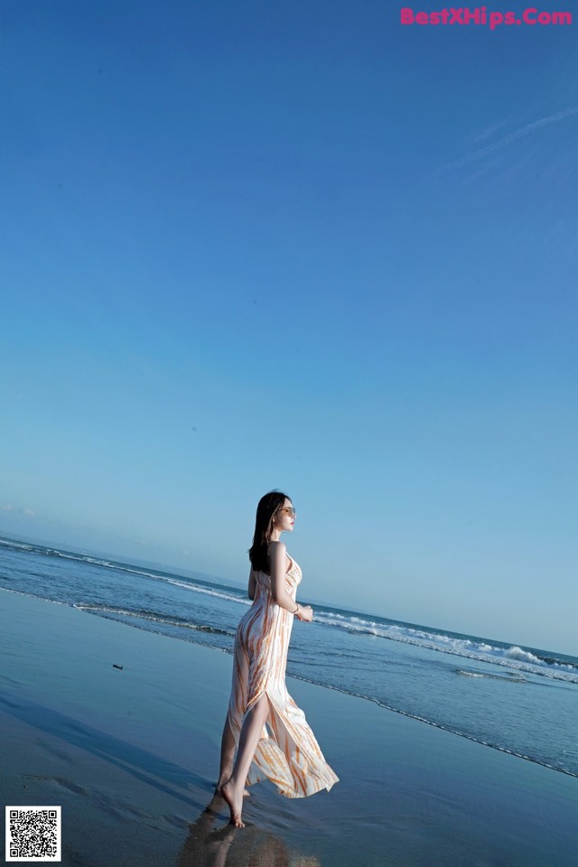 A woman in a long dress walking on the beach.