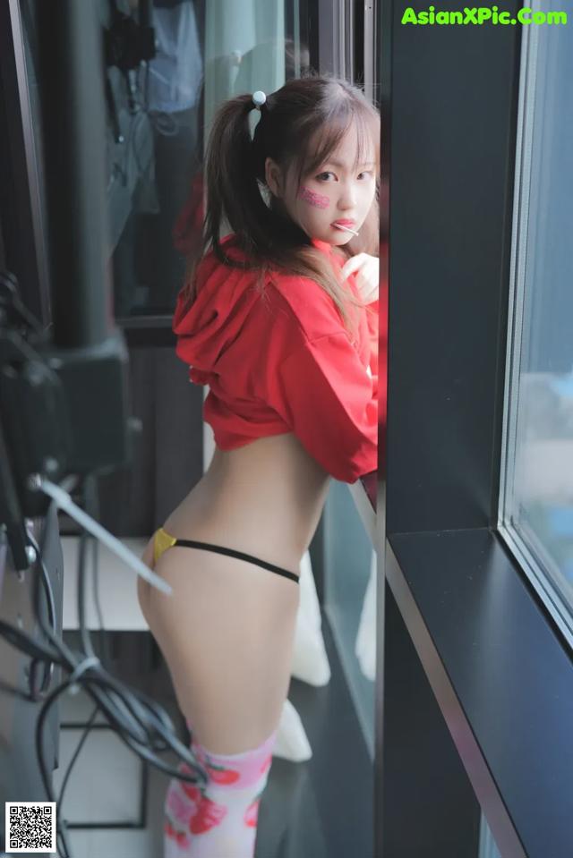 A woman in a red shirt and yellow panties leaning against a window.