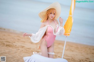 A woman in a pink bikini and a white hat on a beach.