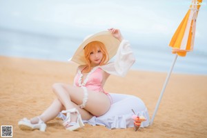 A woman in a pink bathing suit and hat holding an umbrella on the beach.