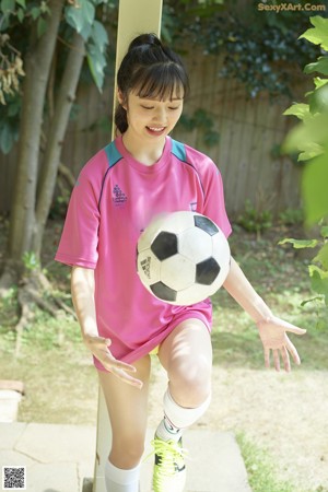 A woman in a pink shirt and yellow shorts kicking a soccer ball.