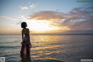 A woman in lingerie standing in the water at sunset.