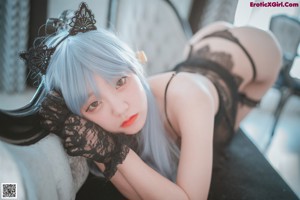 A woman with blue hair wearing a black lingerie on a bed.